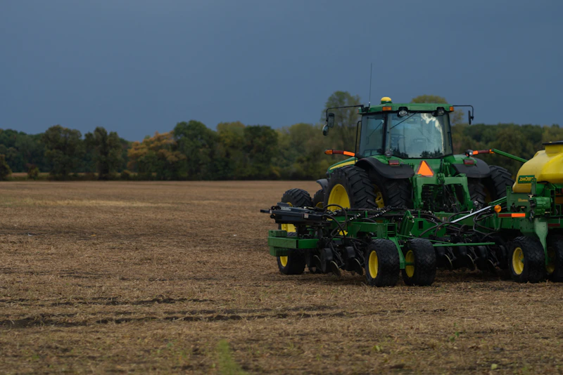 Green and yellow tractor seeding a brown field