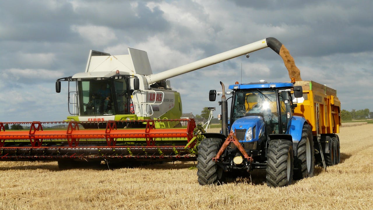 service-04 A modern combine harvester and tractor working together to harvest wheat in a sunny outdoor field.