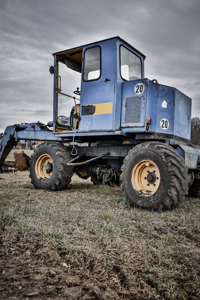 A blue tractor parked on a grassy farm field under a cloudy sky.